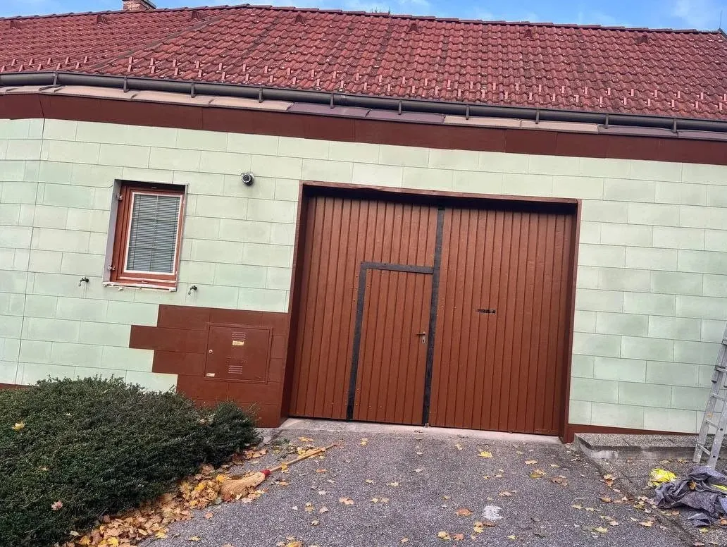 Nachher: Dieselbe Fassade nach der Sanierung: gleichmäßiger Anstrich, neu lackiertes Holztor, abgesetzter Sockel