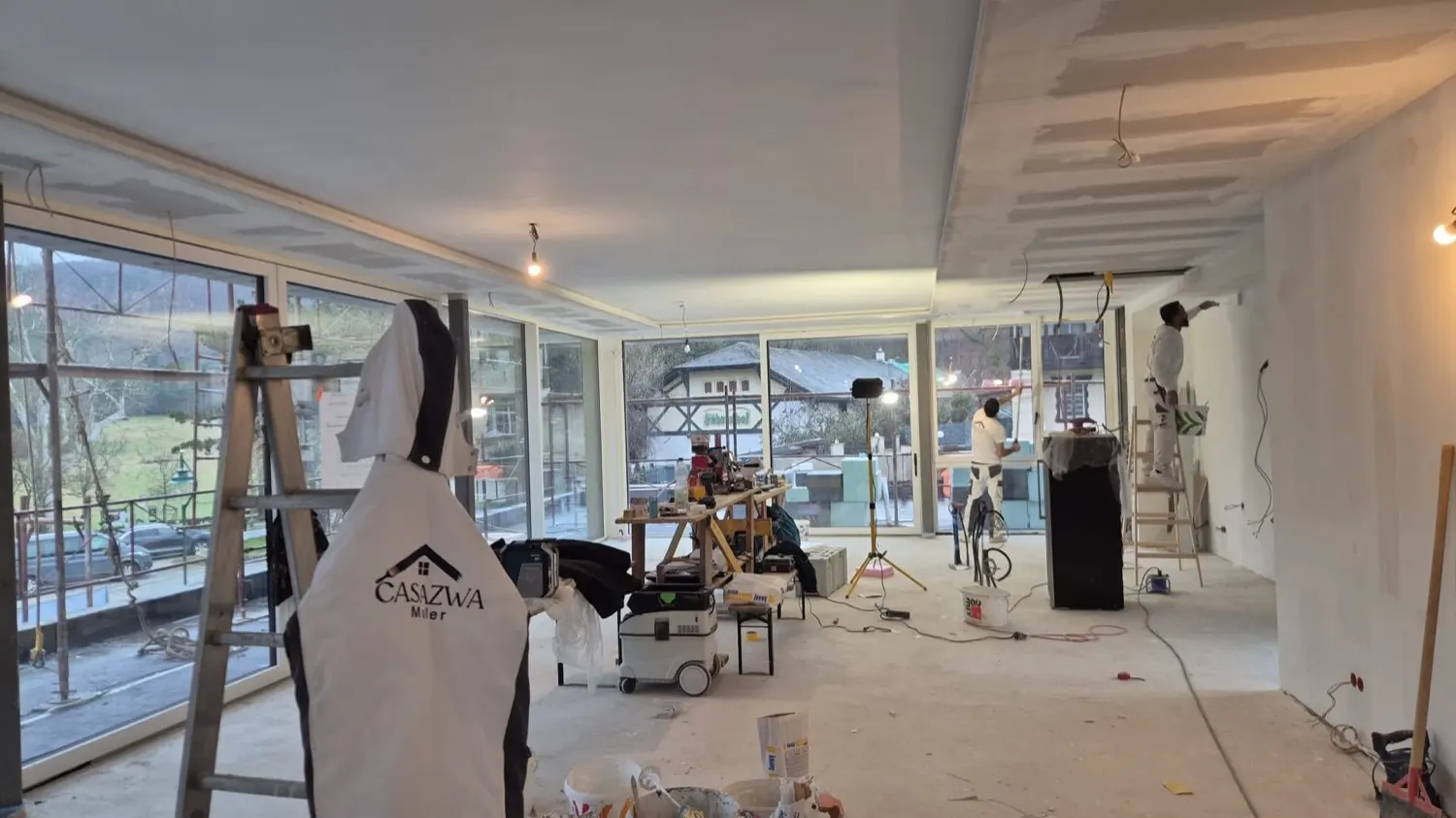 Baustelle mit Casa-Zwa-Arbeitsjacke an der Leiter, dahinter die Fensterfront