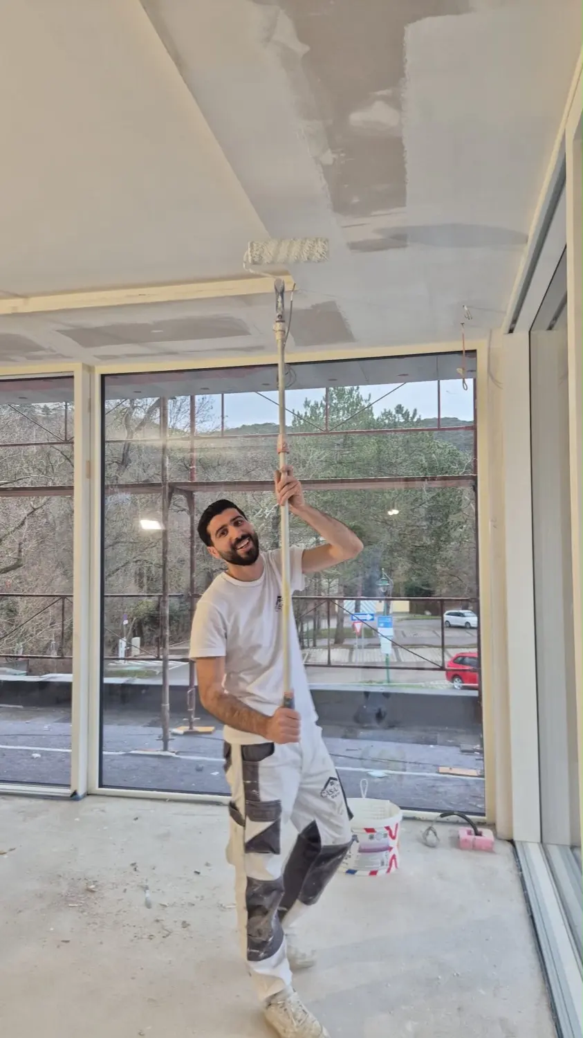 Zaim streicht die Decke mit der Teleskoprolle vor der Glasfront